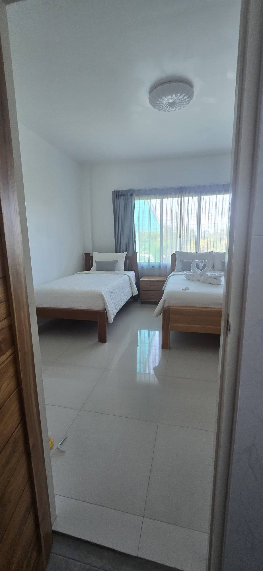 Second bedroom with twin wood beds, white linens and large window