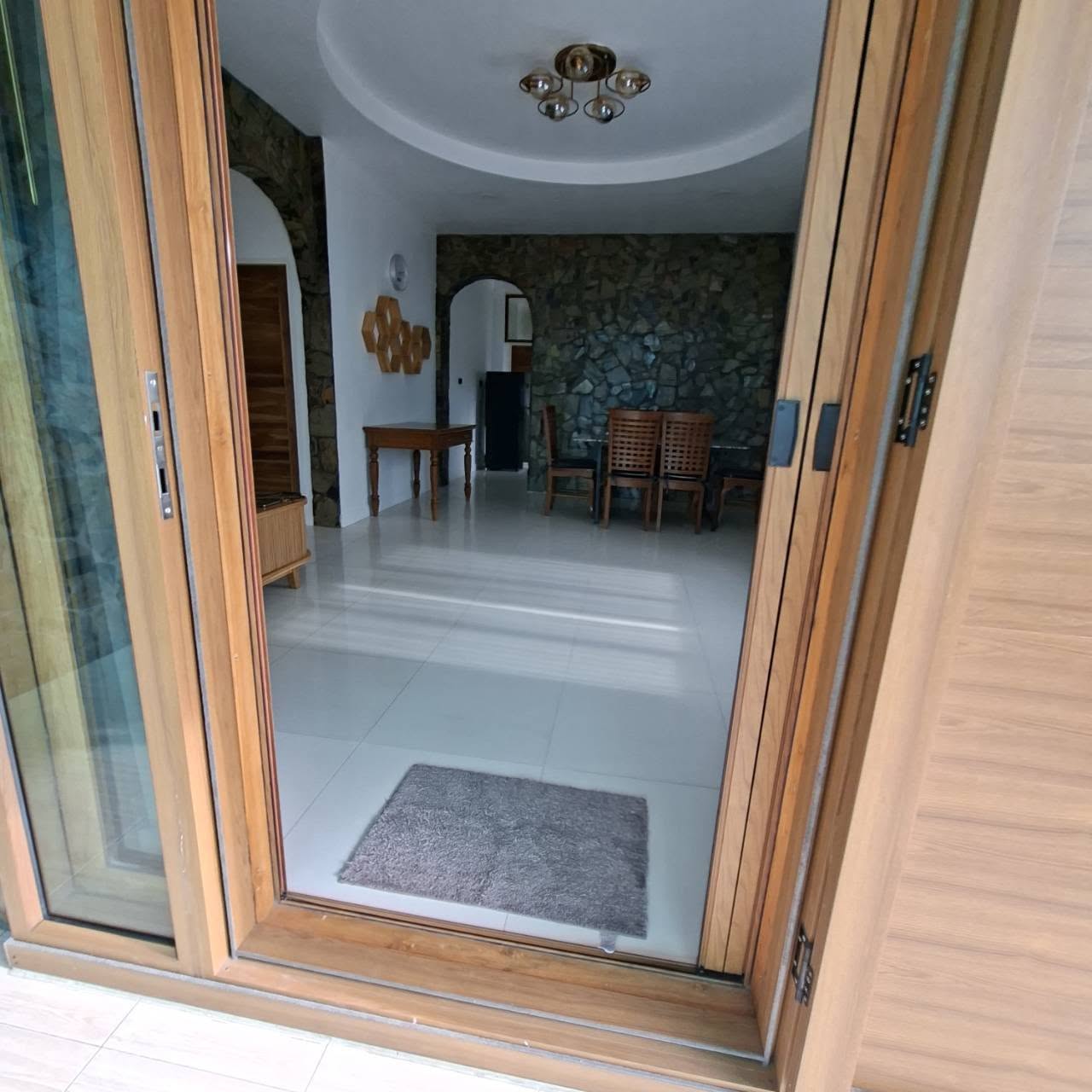 View into dining room through open sliding door with chandelier and stone wall