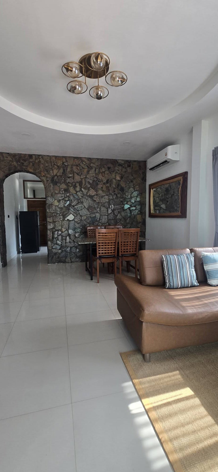 Open living and dining area with brown sofa, wood dining table and stone accent wall