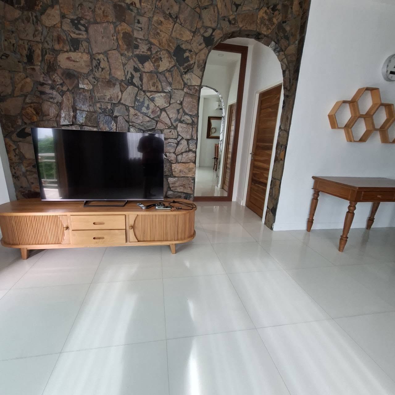 Living area with TV on wood console and natural stone feature wall with arched doorway